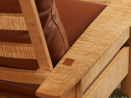 Back side view of a figured maple adjustable back arm chair showing the slatted back and luggage brown leather cushions
