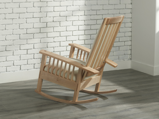 The back and side view of a figured maple rocking chair with soft cream wool upholstery in a room with a gray floor and white tiled wall.