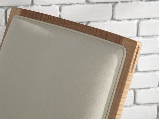 The tight upholstered back of a cream wool and figured maple rocking chair.