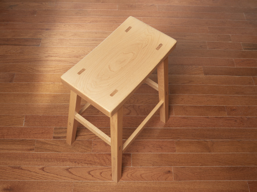 Top angled view of a maple stool showing the seat top with exposed through mortise wedge tenons and splayed legs.