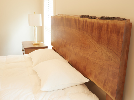 Side view detail of a handmade live edge cherry platform bed in a bright bedroom with white pillows and linens