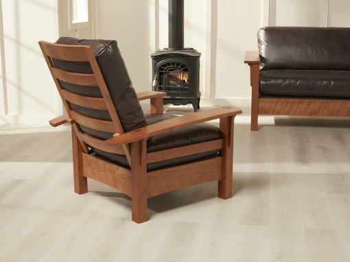 An angled back view of the Coorie adjustable back arm chair in cherry with peppercorn Italian leather cushions shows the slatted back and sides of the arm and chair rails.