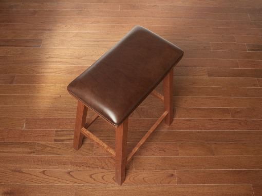 A top angled view of a rectangular cherry barstool with a brown leather seat and squared splayed legs shown on a hardwood floor.