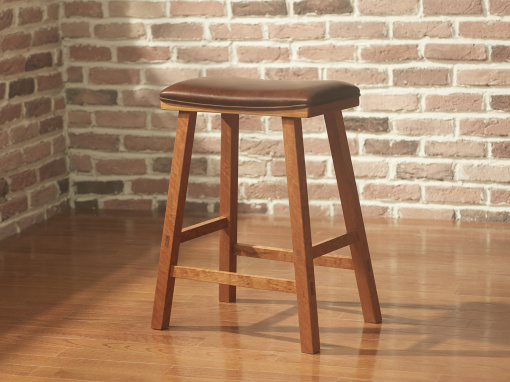 A simple cherry bar stool with a rectangular seat and squared splayed legs with chocolate brown leather upholstery in a room with exposed brick walls and hardwood floor.