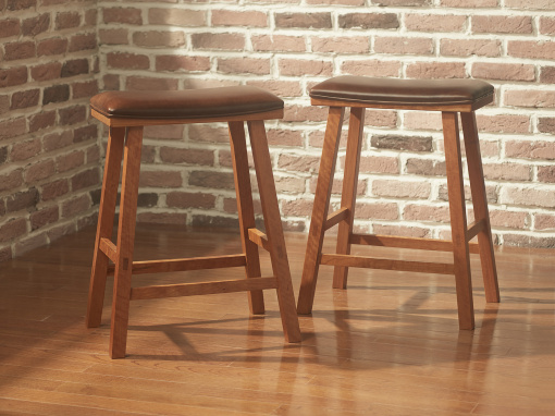 A pair of rectangular upholstered Cherry Kitchen Barstools with brown leather seats and squared splayed legs shown side by side in a room with an exposed brick wall and a hardwood floor.
