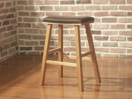 A simple maple bar stool with a rectangular seat and squared splayed legs with Italian leather upholstery in a room with exposed brick walls and hardwood floor.