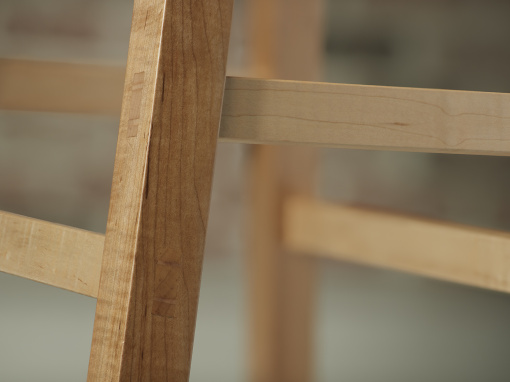 A close up view of the through mortise wedged tenon on the leg of an upholstered maple kitchen barstool.