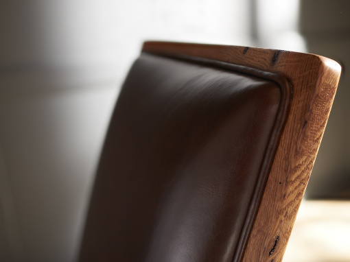 Close-up detail of the backrest on a handcrafted oak rocking chair with rich brown leather upholstery.