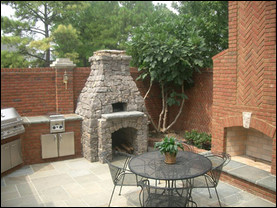 This Memphis outdoor kitchen with brickwork features a Fogazzo wood-fired oven finished in stone, a gas grill, side burner, slate countertops and an outdoor fireplace. Photo <br />© Fogazzo Wood Fired Ovens and BBQs