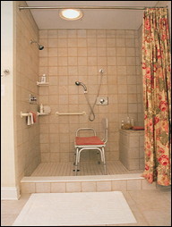 This is an accessible transfer shower with a raised dam that keeps water inside the stall. The homeowner transfers from his wheelchair to the portable seat. From this position, he regulates the water temperature from the rear-wall mixing valve and directs the flow with the handheld spray.